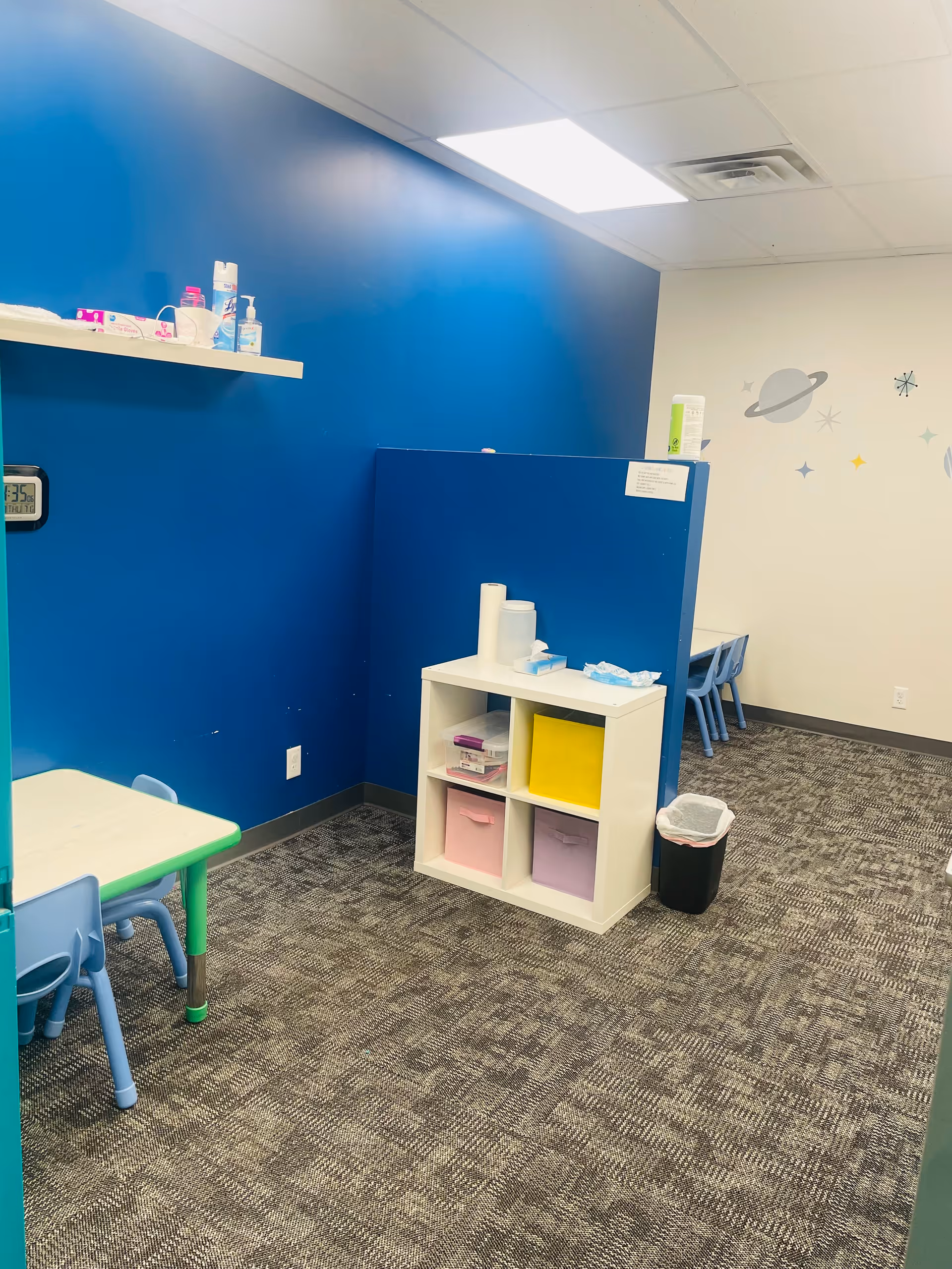 Bright blue-walled playroom with cubby storage, small tables, and space-themed decor.