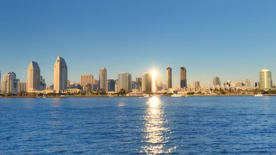 Sunlit city skyline across calm water under a clear blue sky