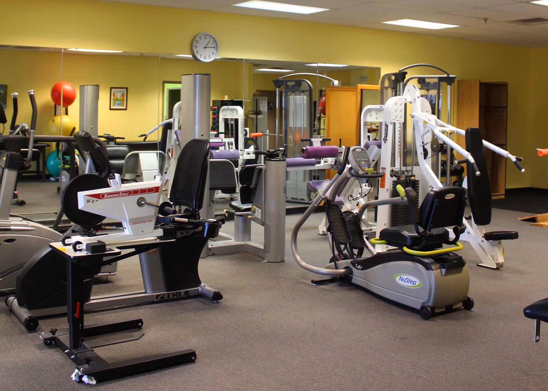 Interior of a senior living facility gym with various exercise machines and mirrors.