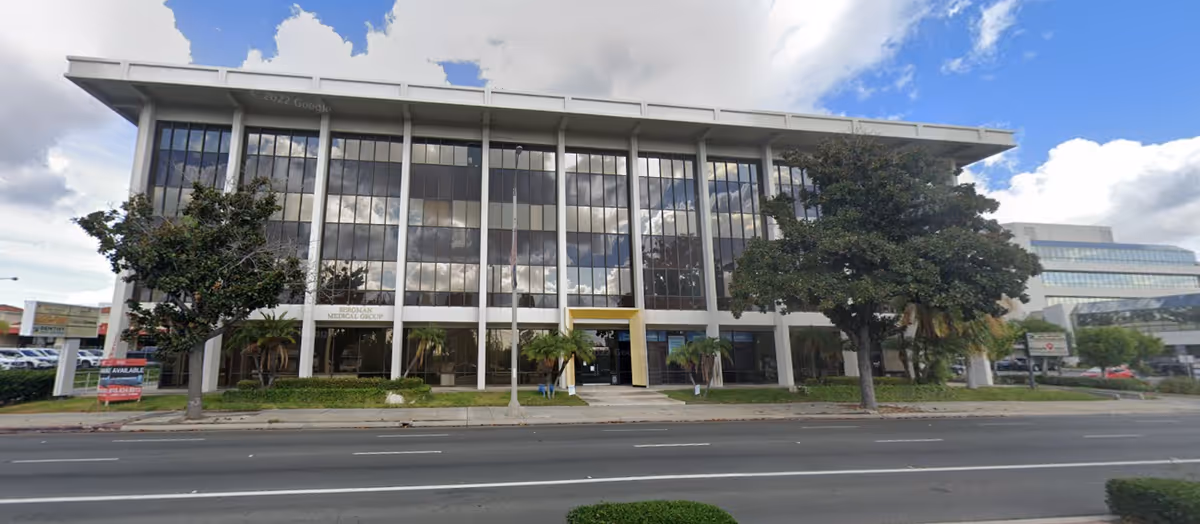 Glass-front, three-story medical facility exterior along a street with trees.