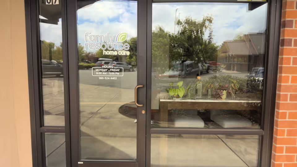 Glass entrance of Family Resource Home Care with logo, hours, and reflections of a parking lot.