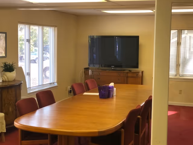 A dining room with a long wooden table, chairs, and a TV on a cabinet.