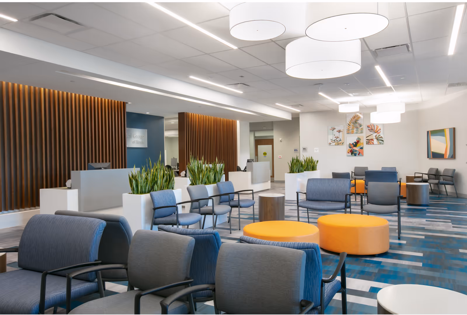 Modern outpatient lobby with blue seating, orange ottomans, planters, and contemporary lighting.