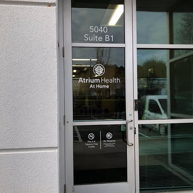 Glass entrance door displays Atrium Health At Home signage and 5040 Suite B1.