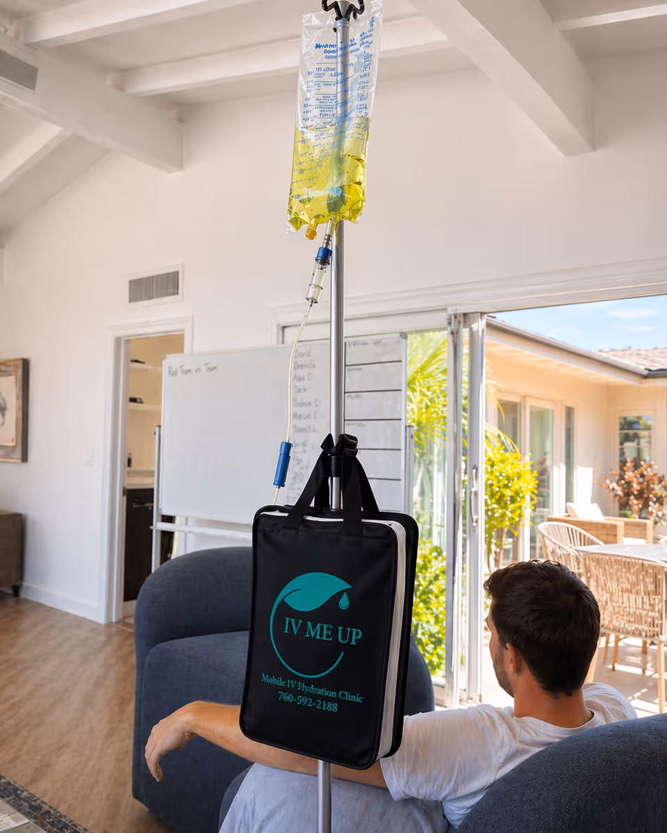 Man seated on a blue sofa with IV bag and pole in a bright living room.