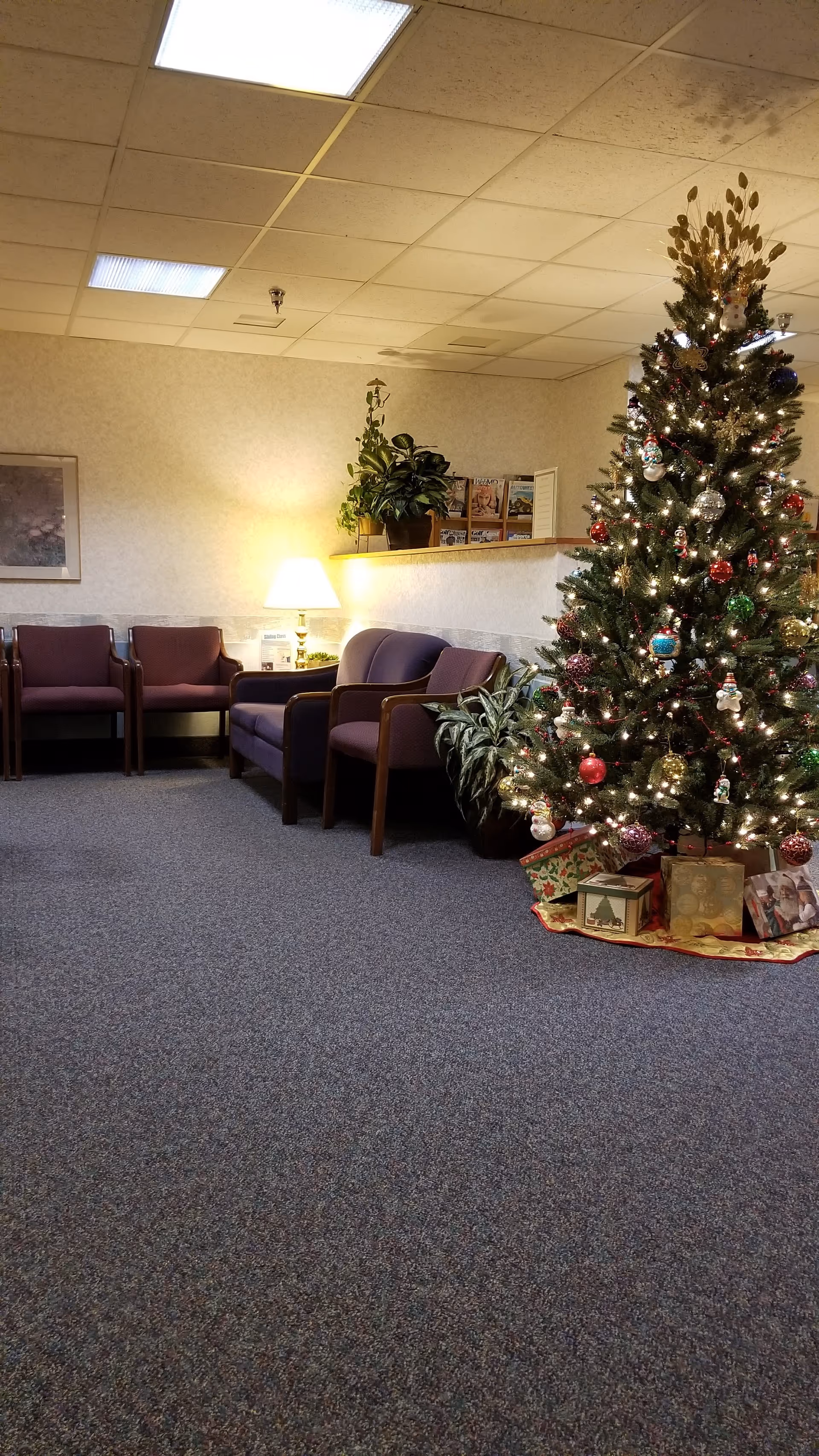 Holiday-decorated waiting area with a Christmas tree, purple chairs, plants, and magazines.
