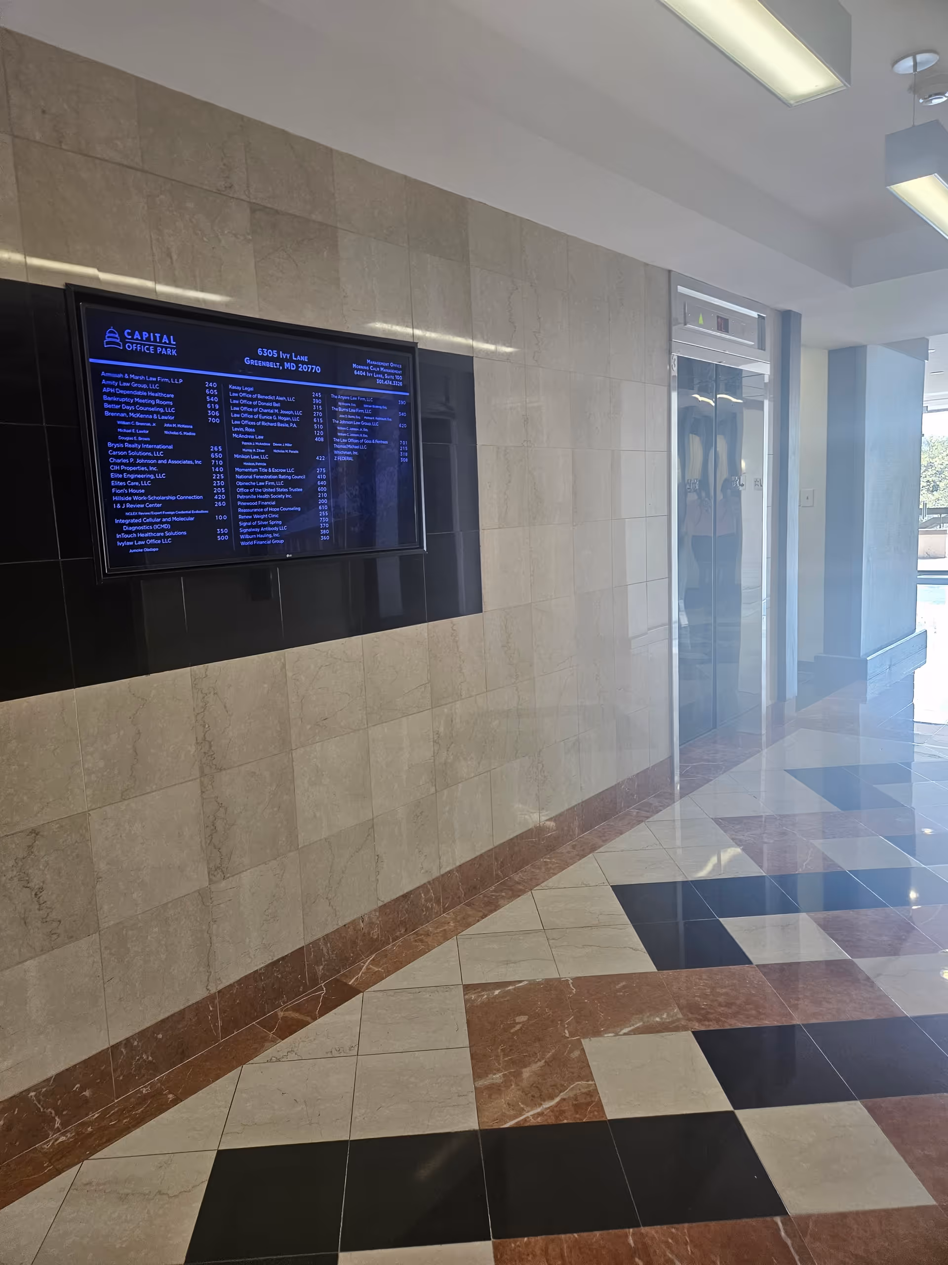 A polished lobby hallway features a digital directory and an elevator by tiled walls.