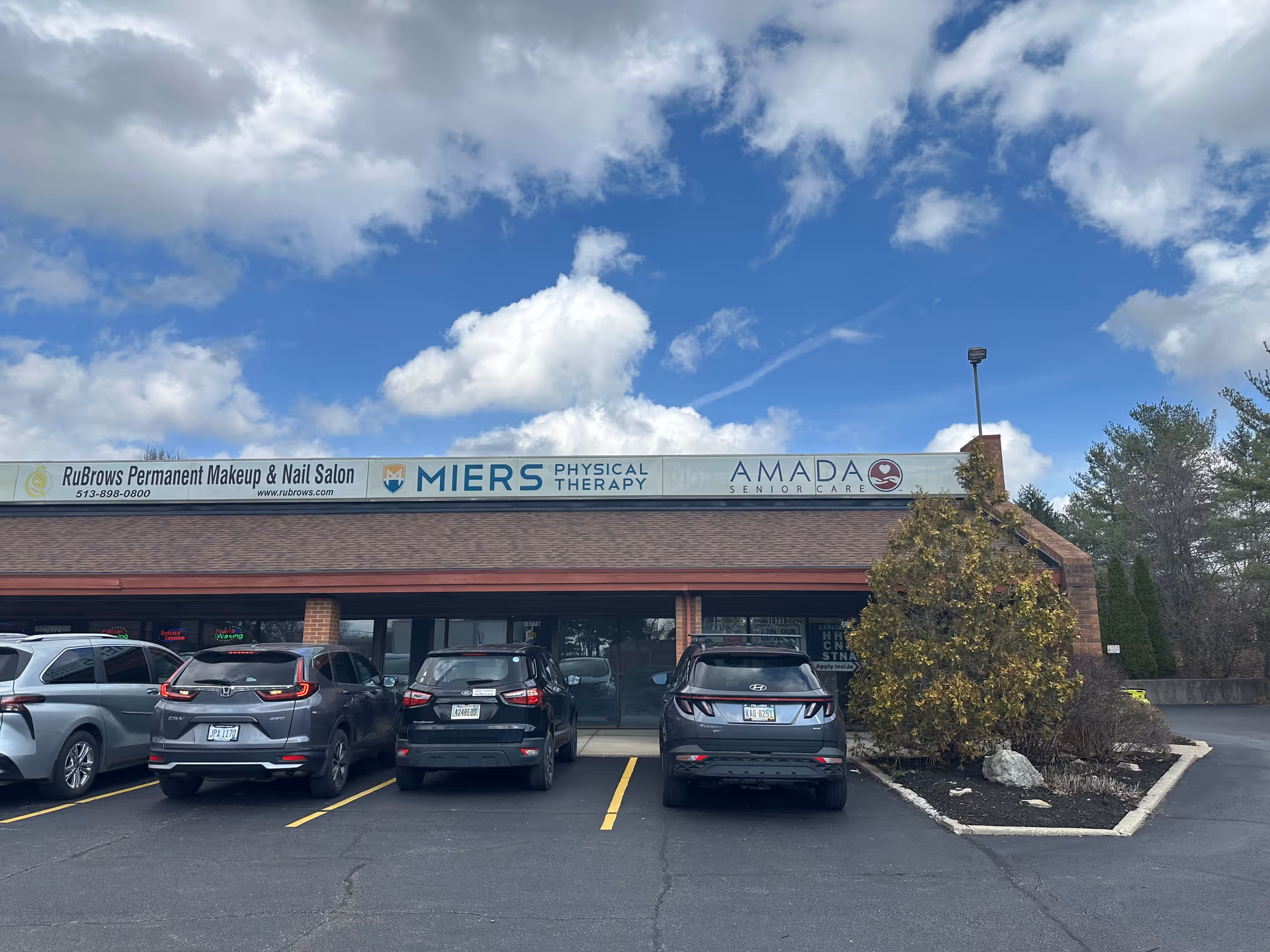 Exterior view of a strip storefront with Amada Senior Care signage and parked cars.