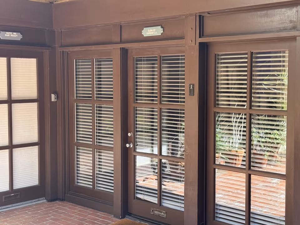 Brown doors with glass panes, blinds, and labeled suites along a hallway.