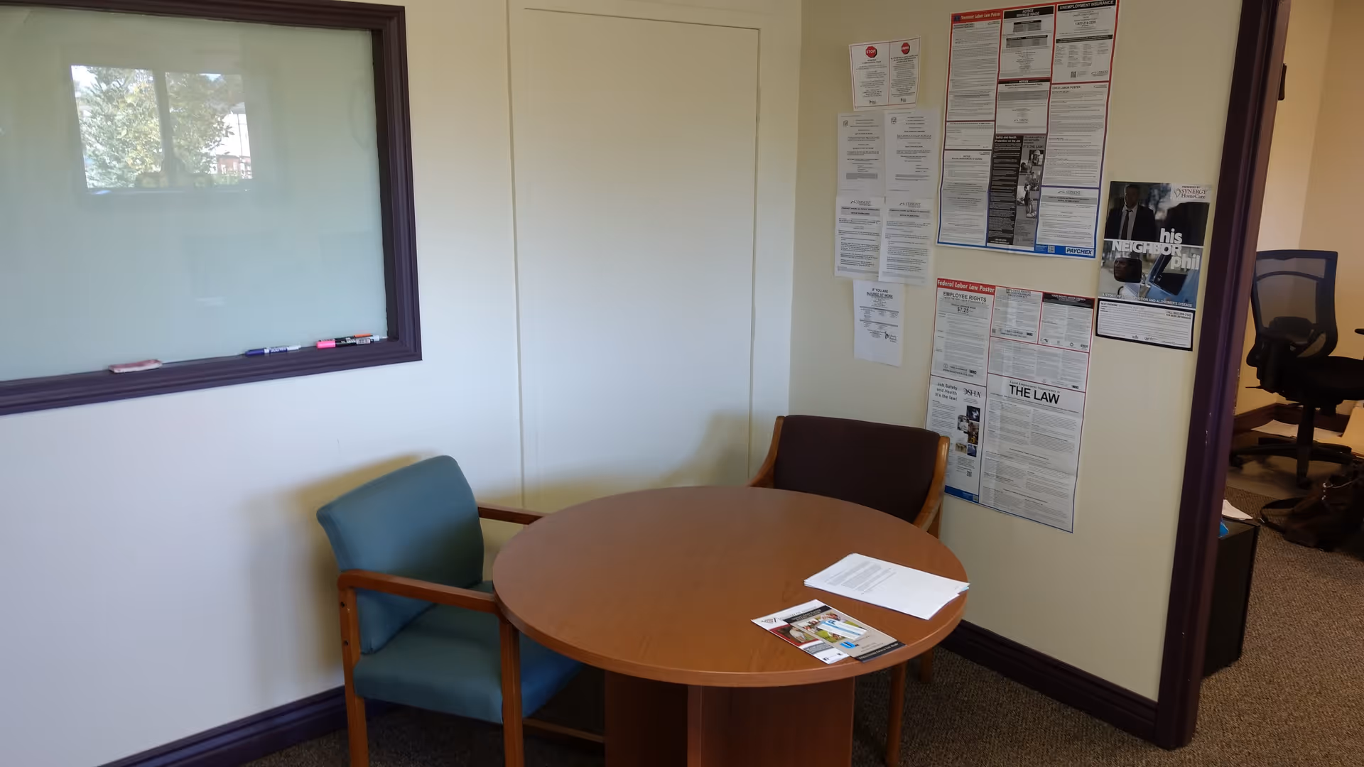 Round wooden table with two chairs and bulletin boards on the wall.