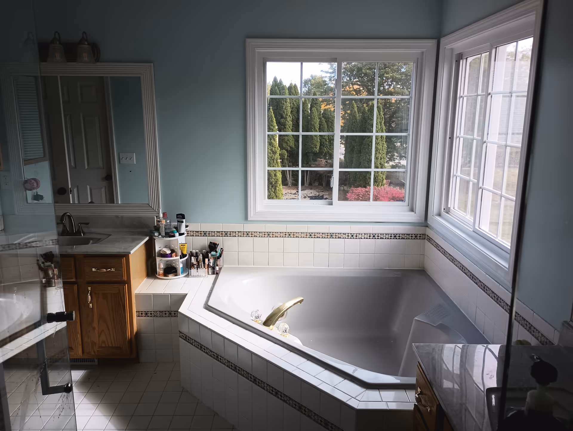 Bright bathroom with built-in tiled tub, vanity, and a large window overlooking greenery.