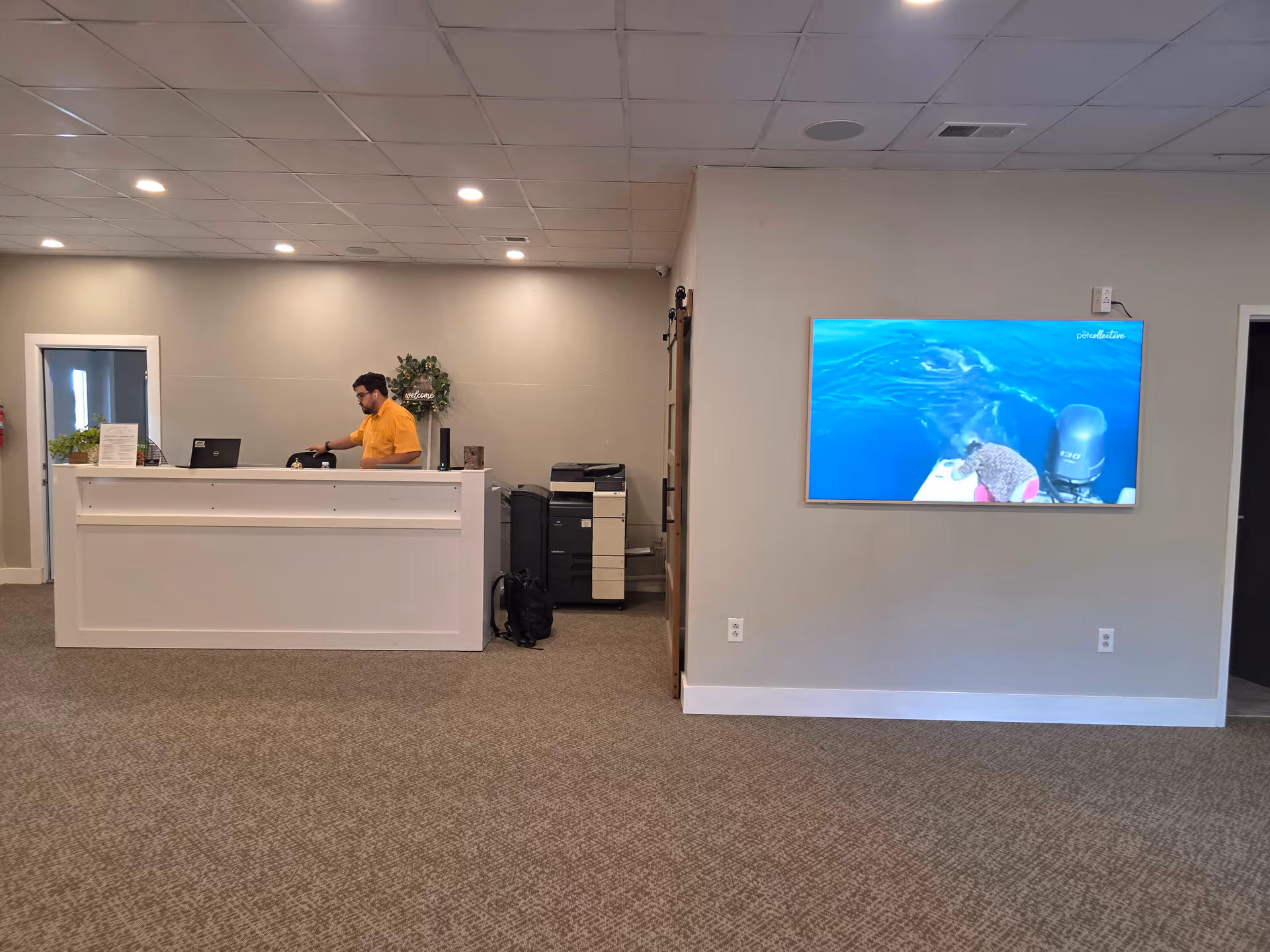 Reception desk area with staff at counter and a large TV mounted on the wall.