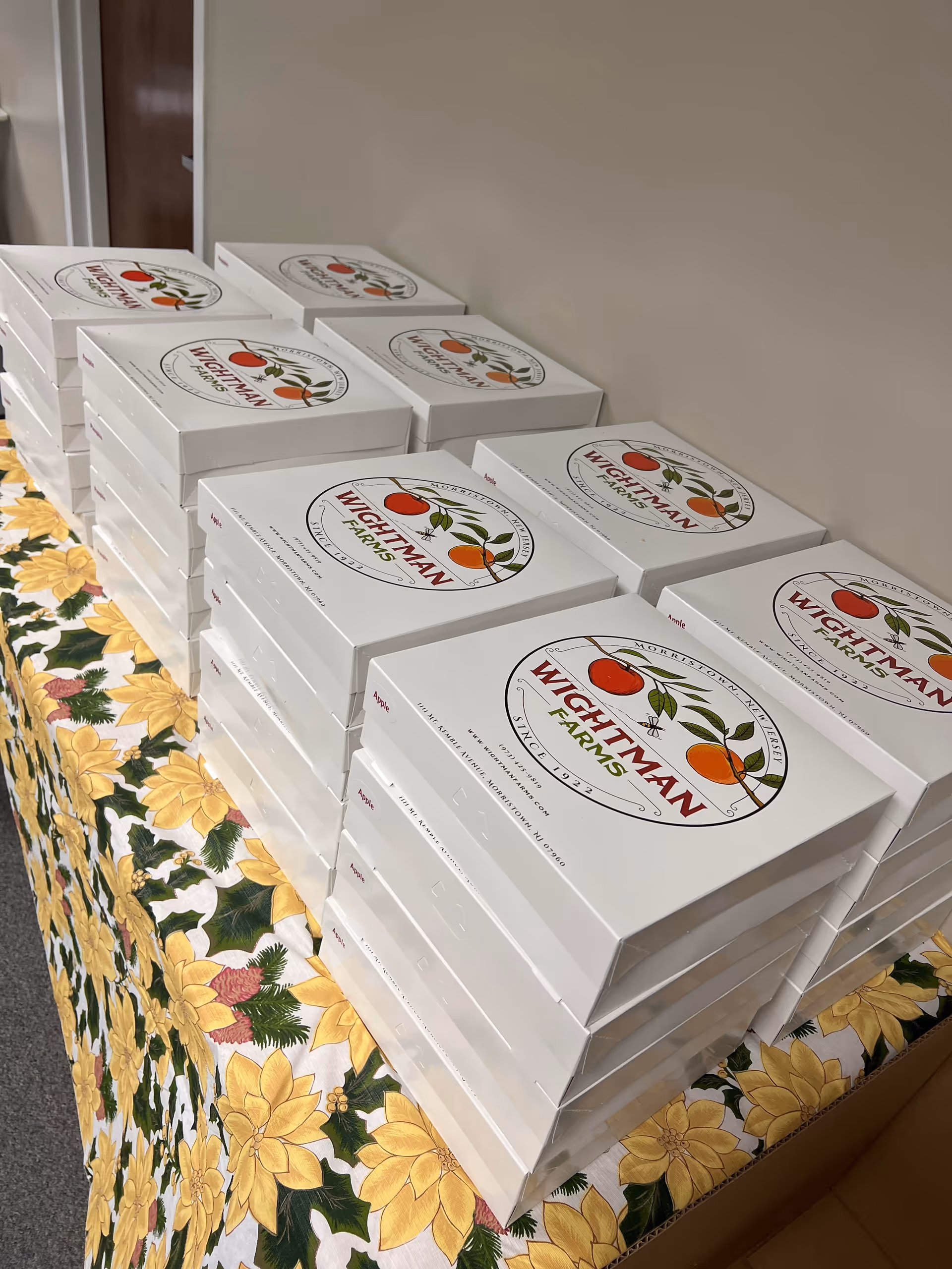 Stacks of white Wightman Farms boxes arranged on a table with a floral tablecloth.