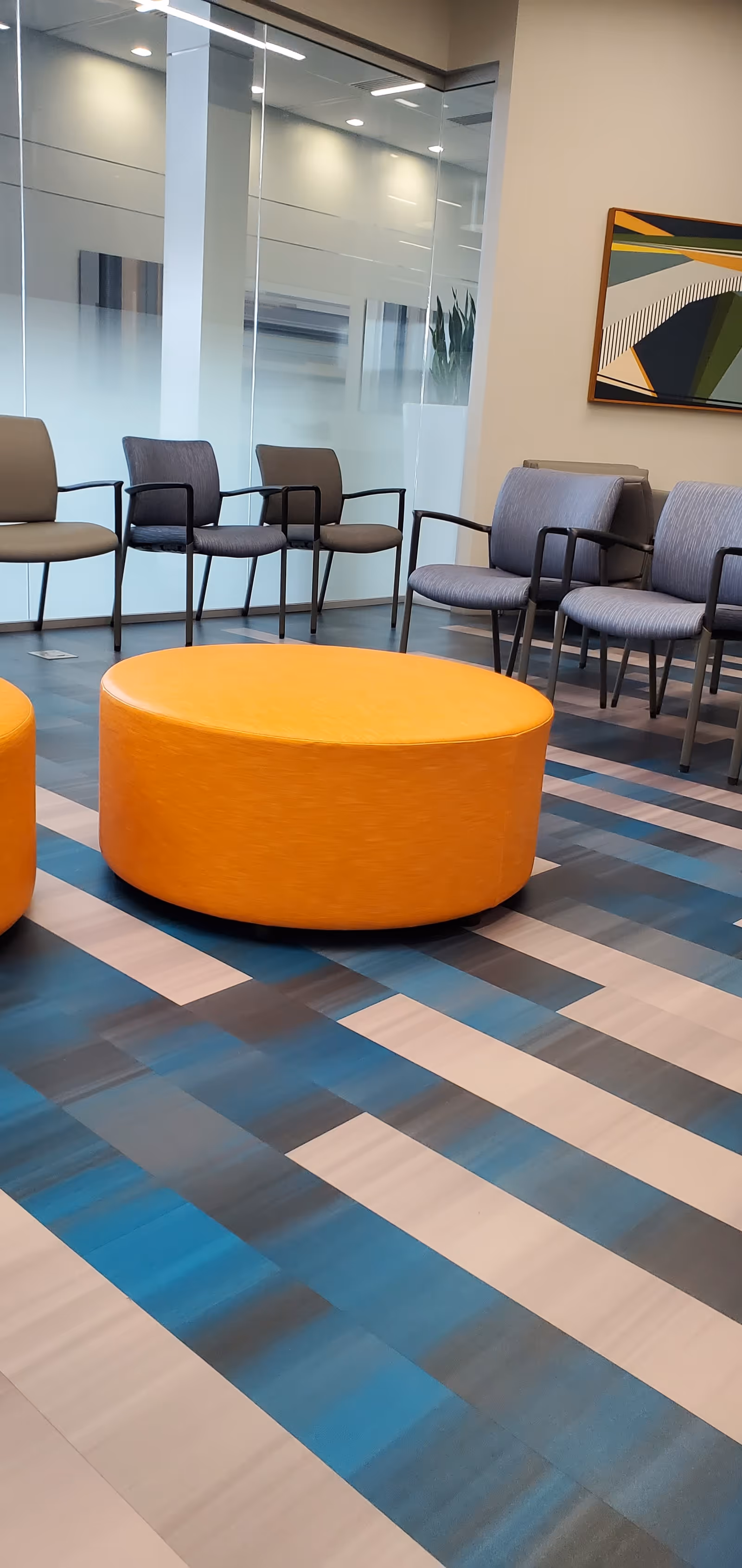 Modern waiting area with blue striped floor, orange ottomans, and gray chairs.