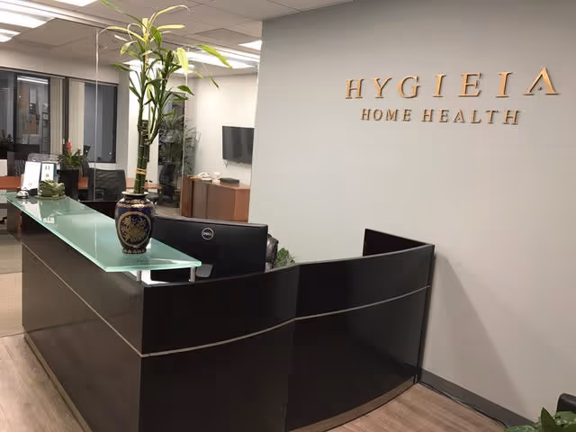Interior reception area of Hygieia Home Health with a curved black desk and potted plant.