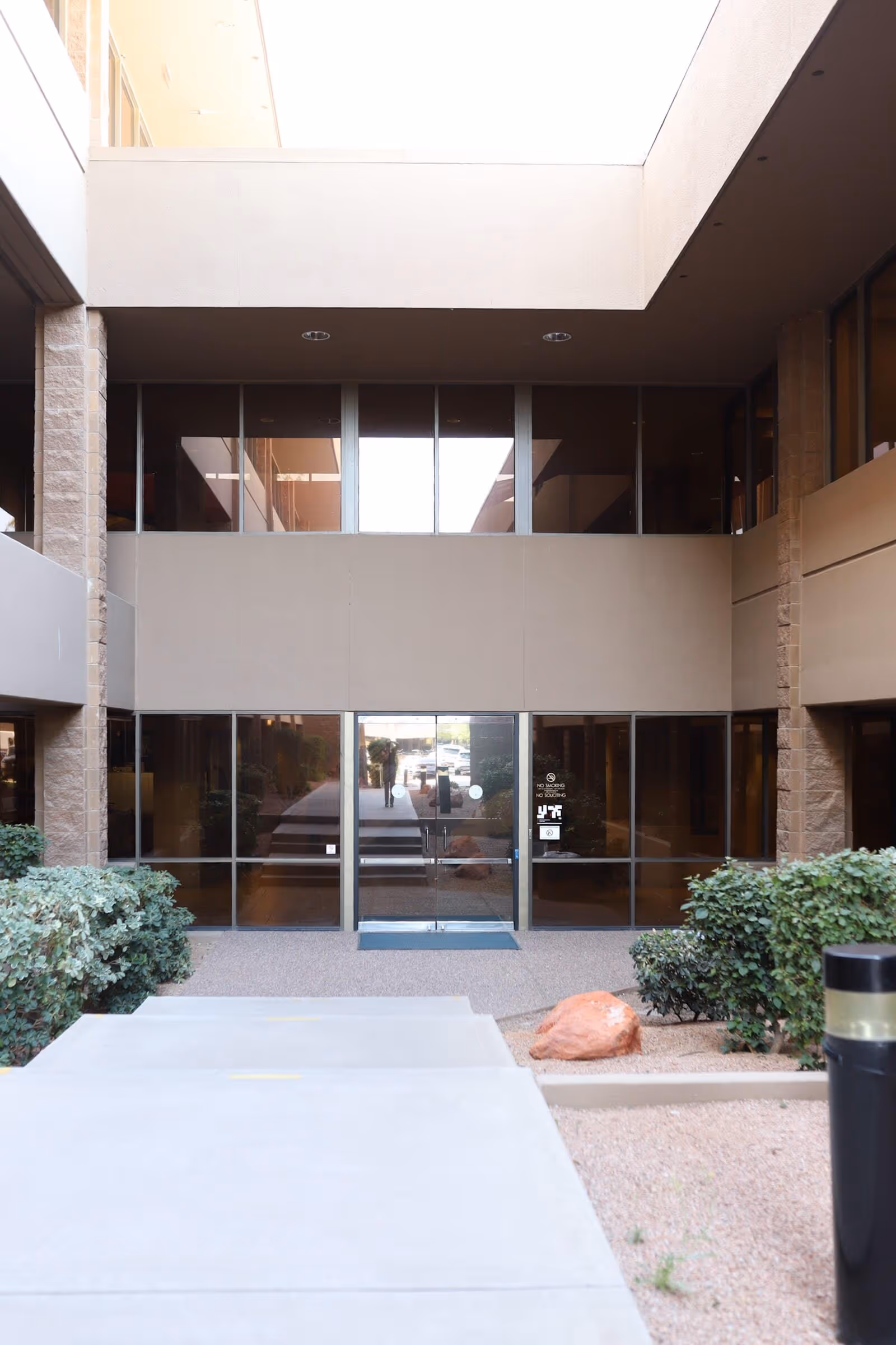 Modern building entrance with glass doors, walkway, and desert landscaping at a senior living facility.