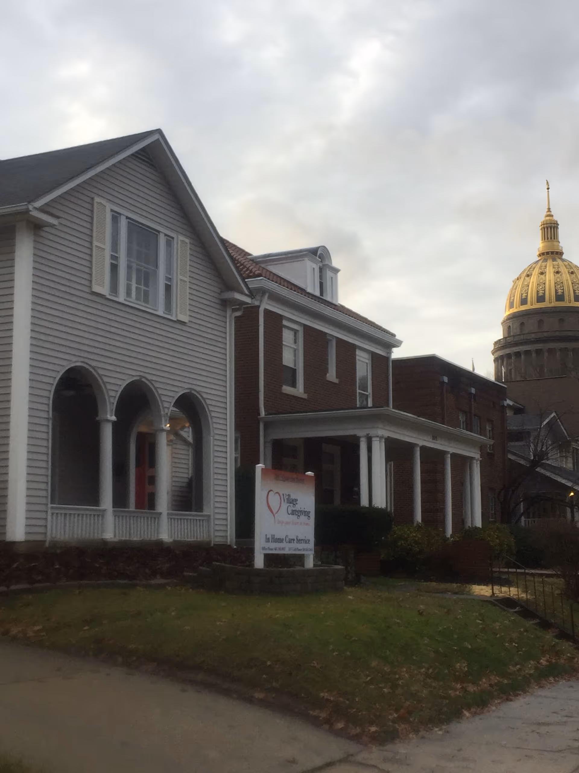 Exterior view of Village Caregiving facility with a two-story building and sign in front.