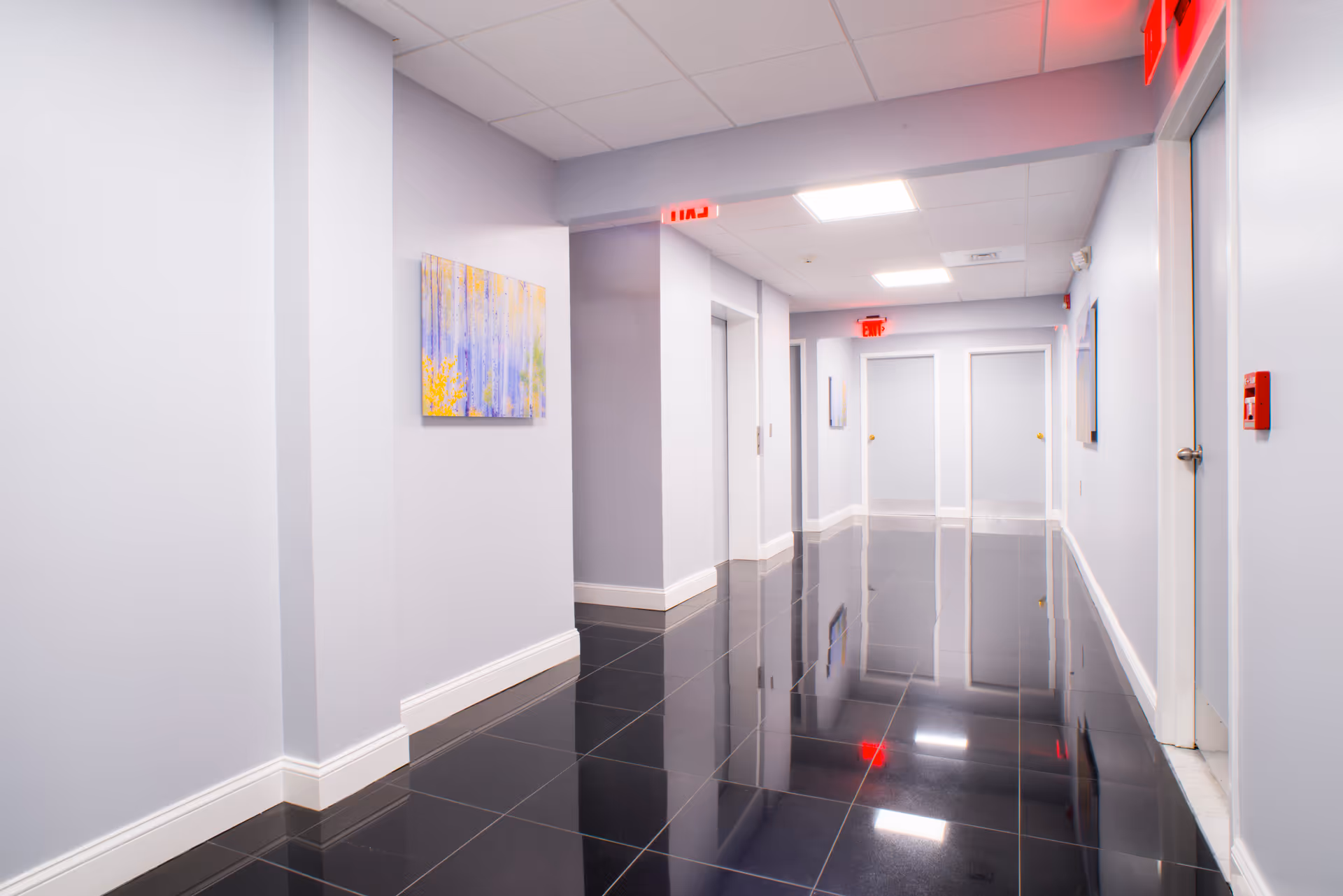 Long, glossy hallway with doors, artwork, and bright ceiling lights in a modern senior facility.
