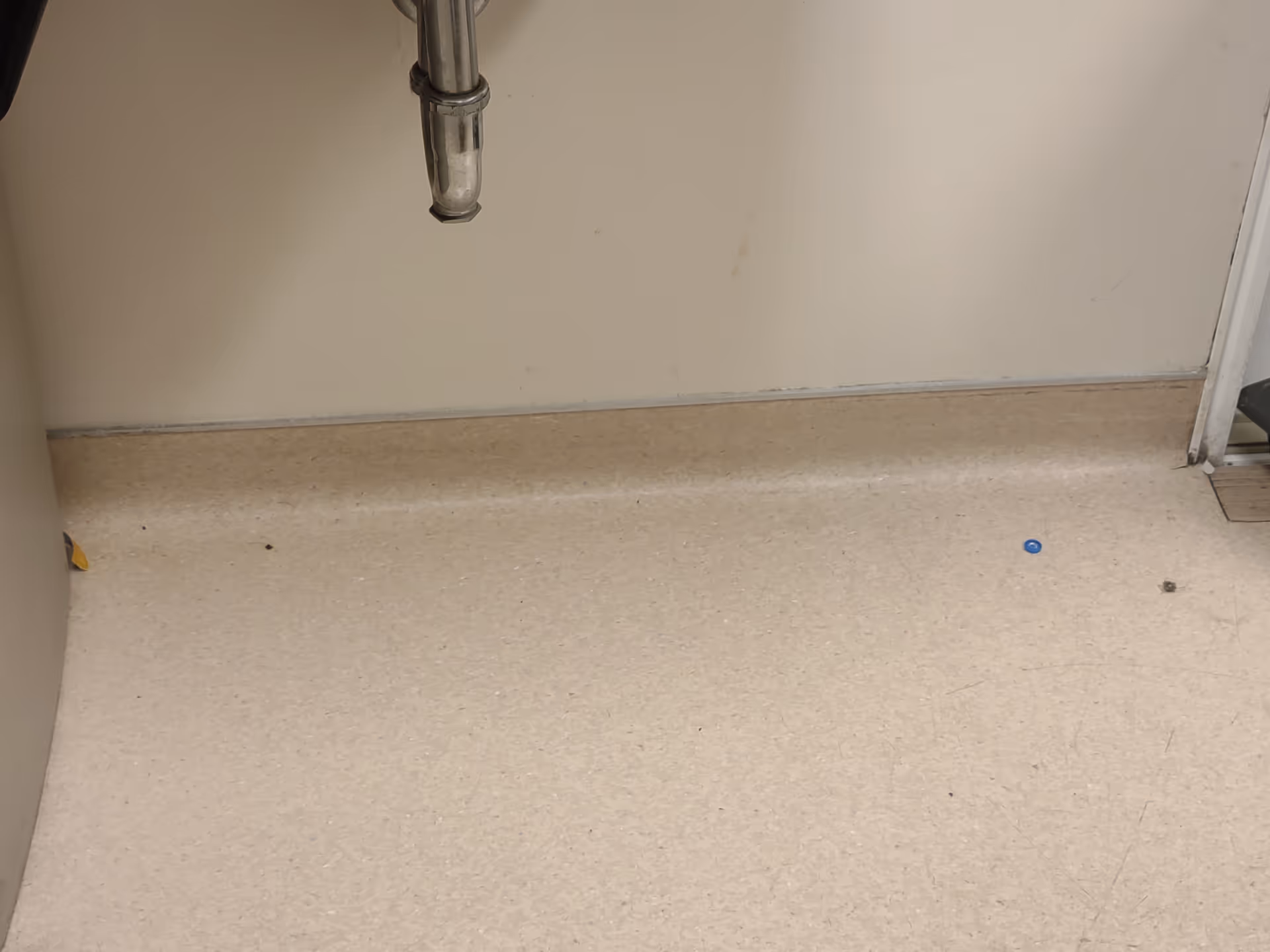 Under-sink plumbing visible in a small bathroom with beige linoleum floor.