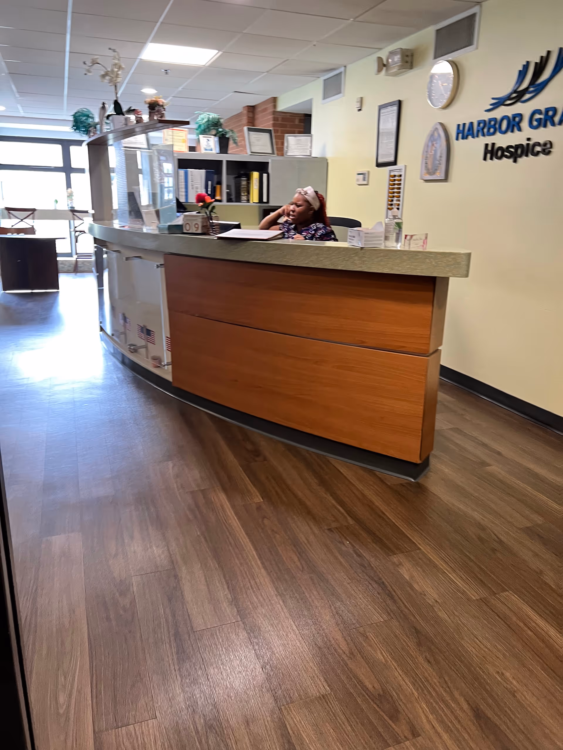 Inside Harbor Grace Hospice lobby, a receptionist sits at a curved wooden desk.