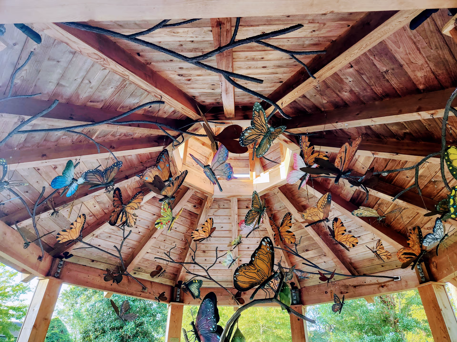 Wooden gazebo interior decorated with colorful butterflies hanging from branches.
