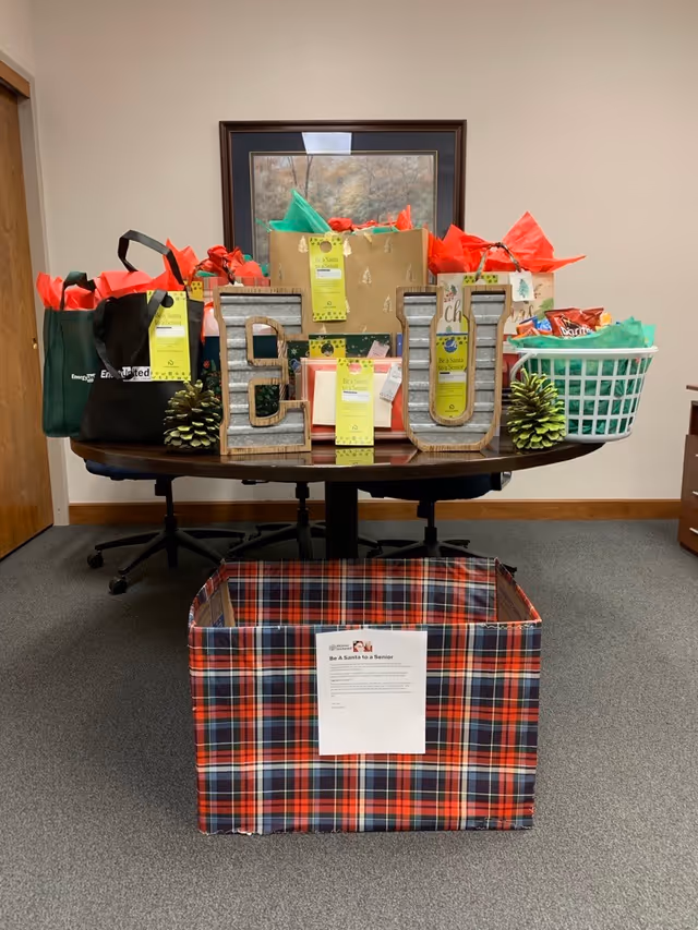 Gift-filled round table inside a Home Instead office, with colorful bags and plaid box.