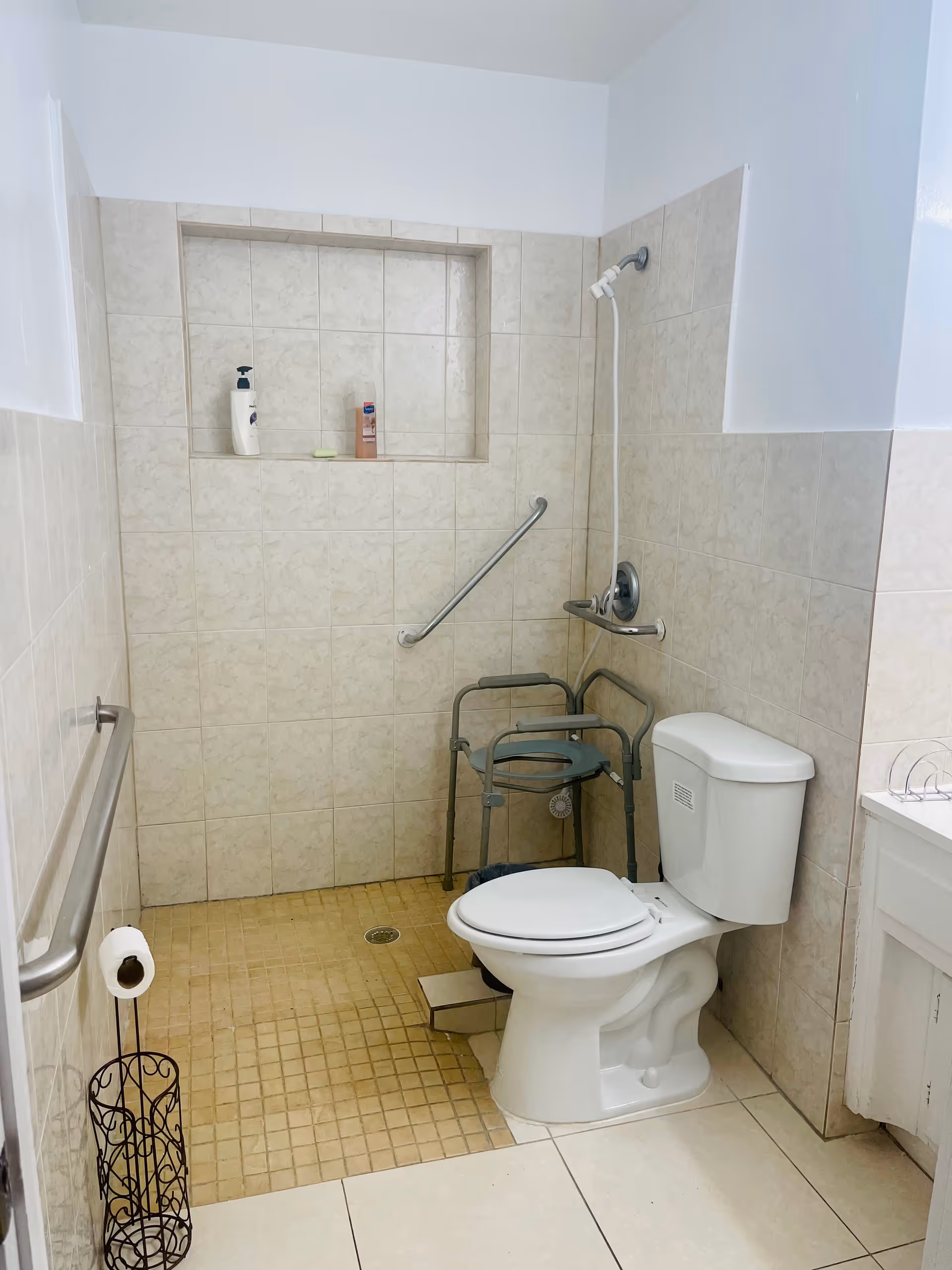 Accessible bathroom with toilet, walk-in shower, grab bars, and tiled walls.