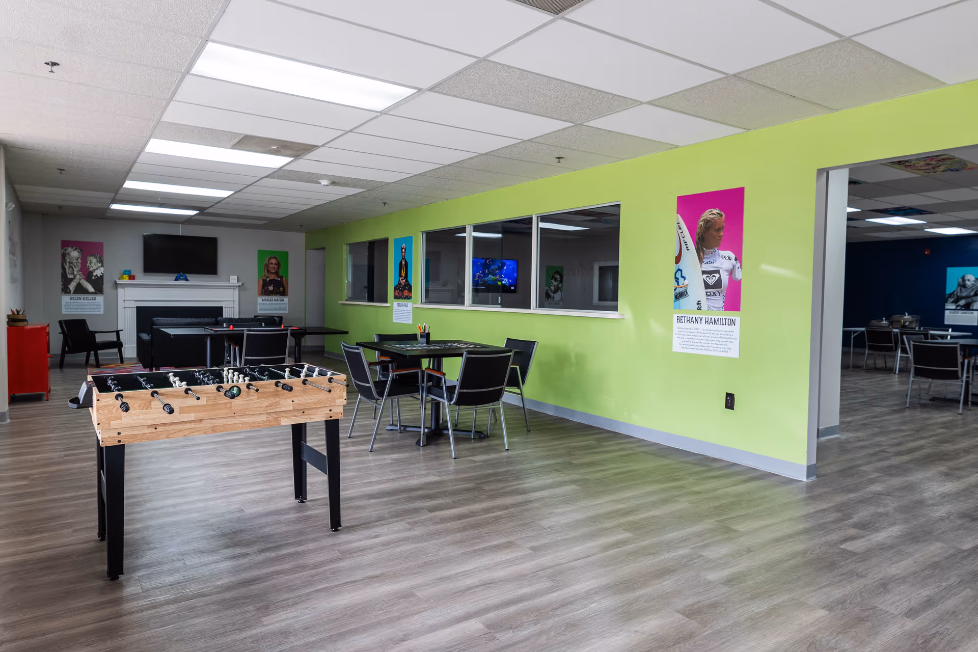 Interior recreation room with foosball table, seating, lime-green wall, posters, and a fireplace.