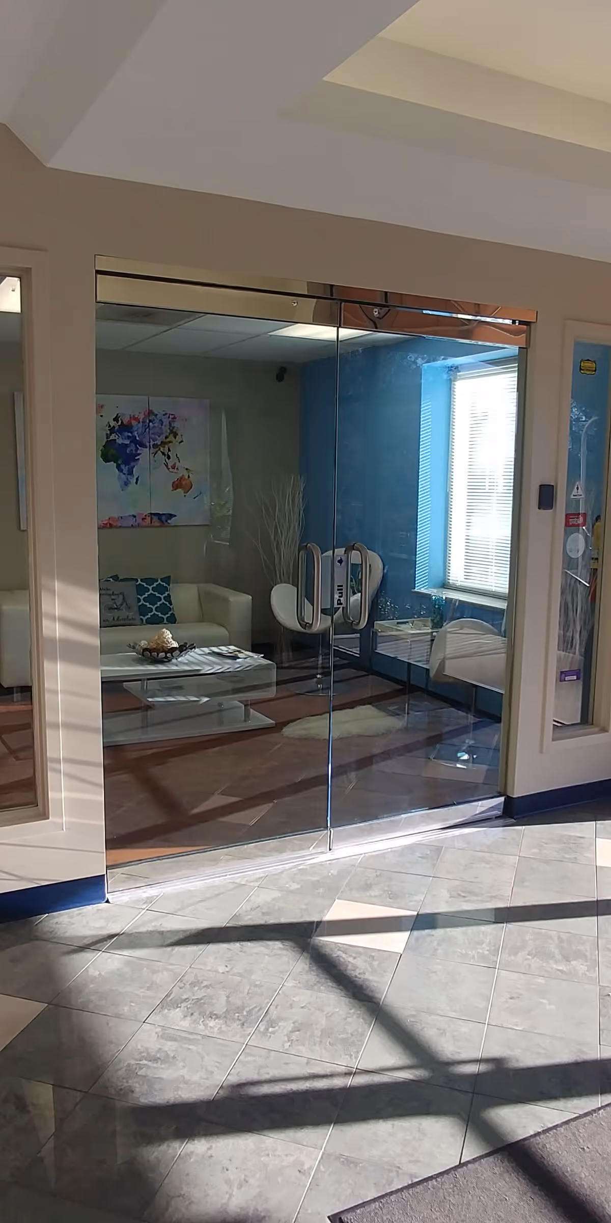 Glass double doors open into a blue-walled lounge with white seating and world map art.