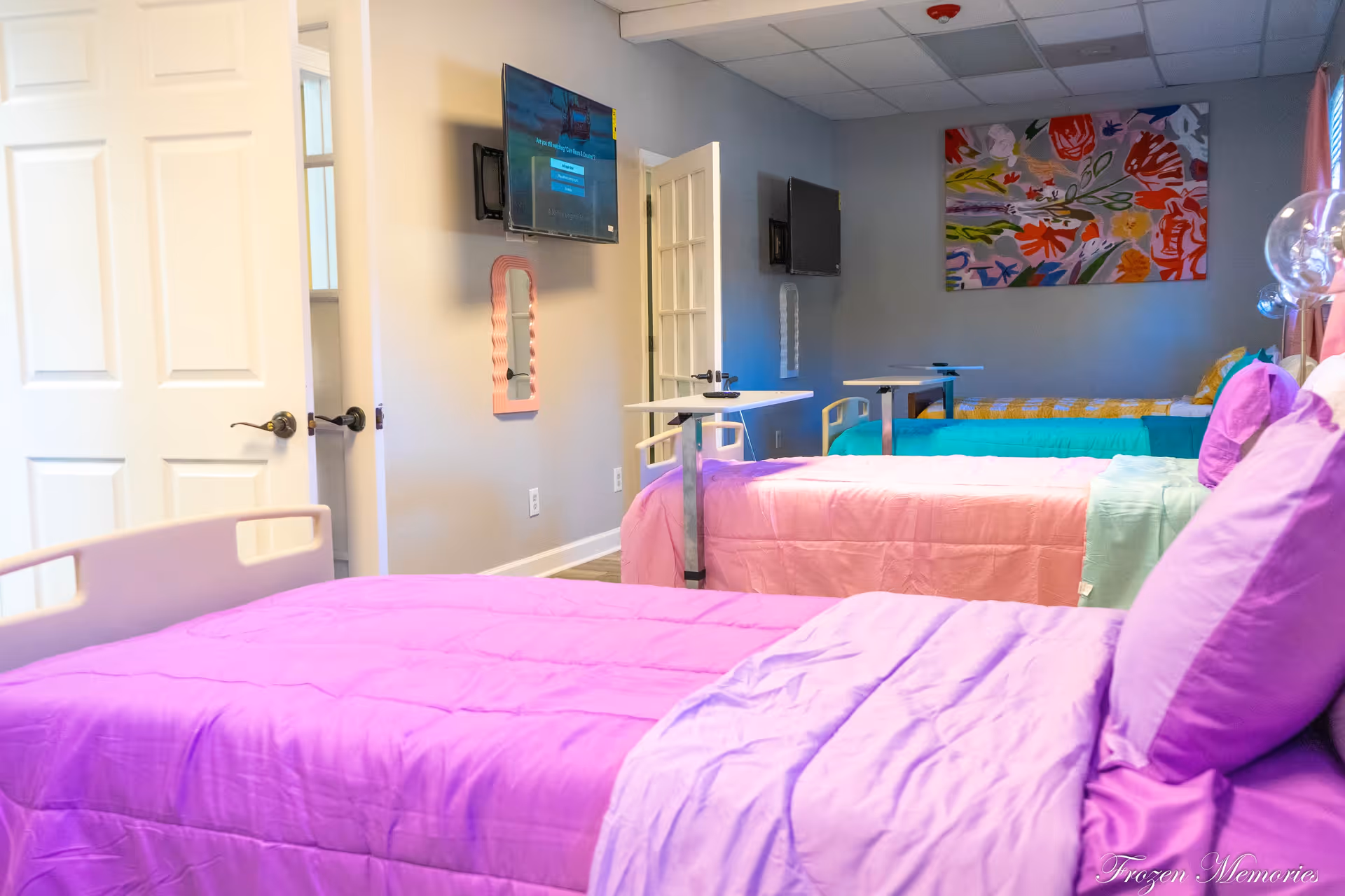 Colorful shared bedroom with multiple beds, purple-pink blankets, and wall art.