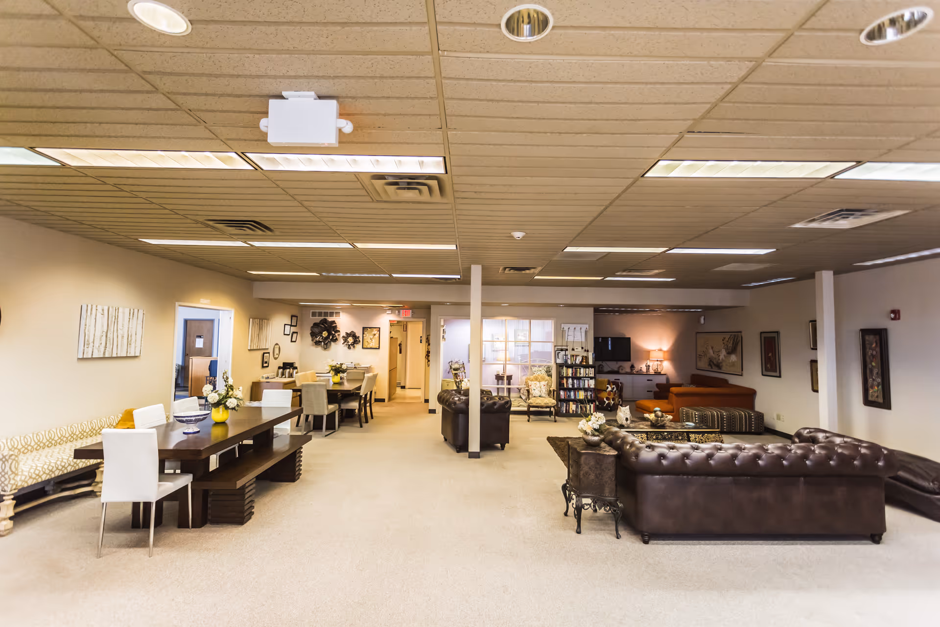 Spacious senior living lobby with sofas, tables, chairs, and bookshelves in warm lighting.
