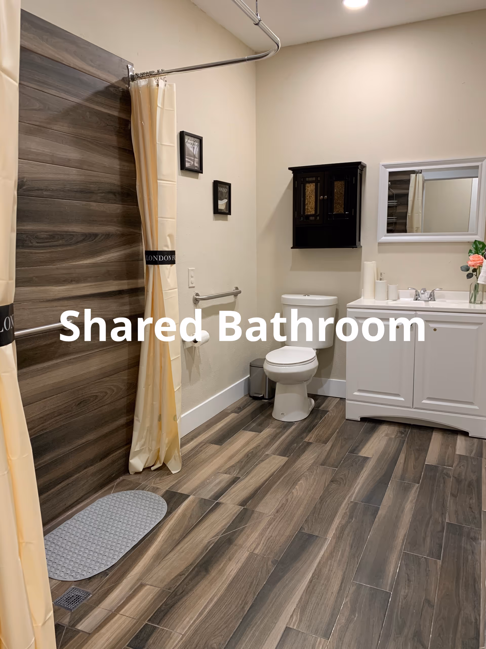 Shared bathroom with shower, toilet, sink, mirror, and neutral decor.