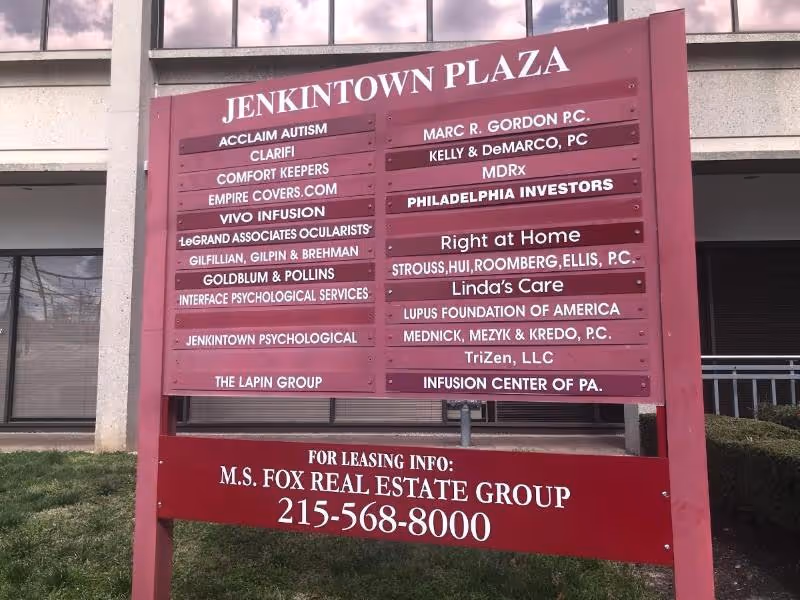 A large maroon directory sign outside Jenkintown Plaza listing Right at Home among tenants.