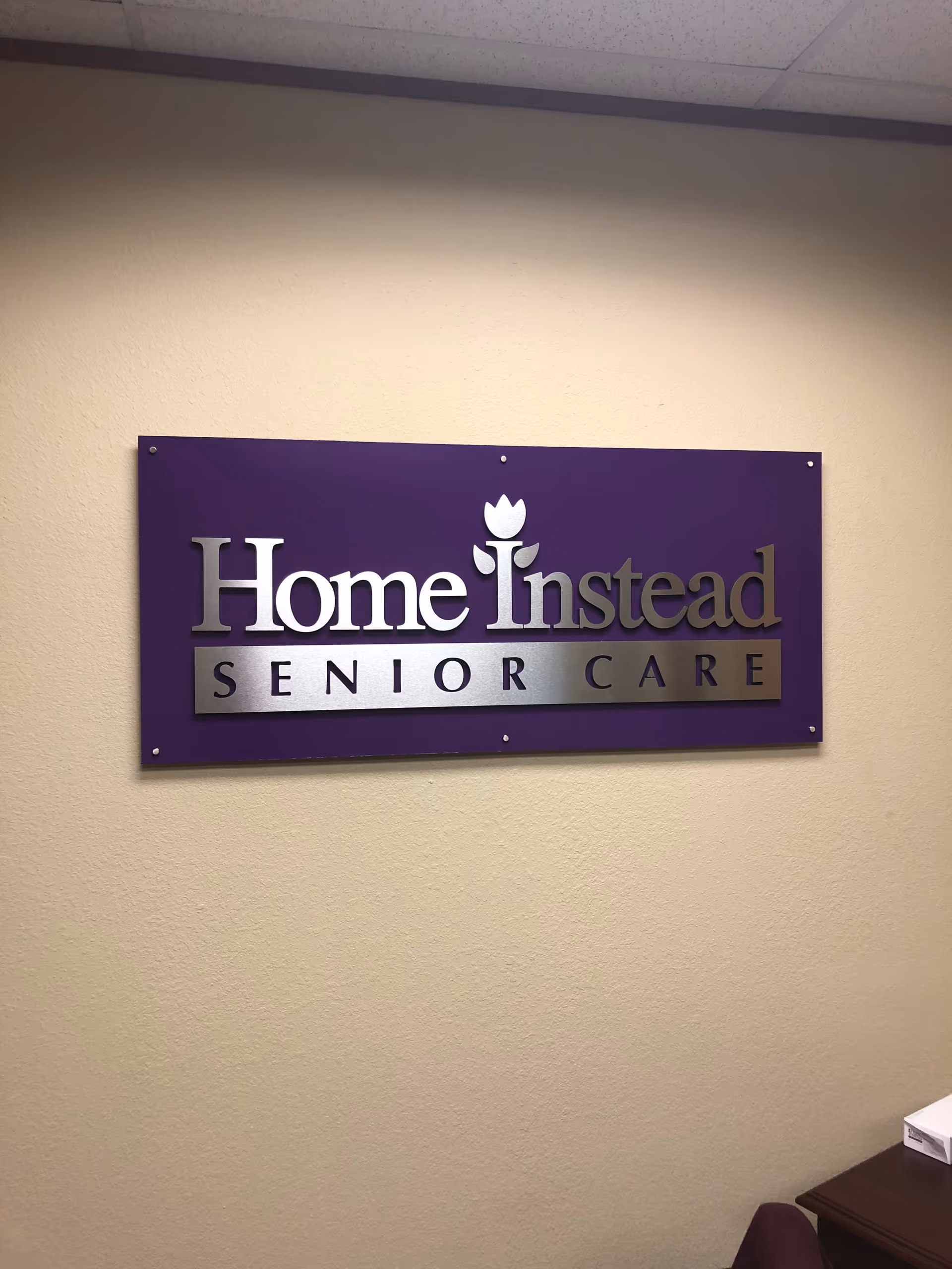 Purple Home Instead Senior Care sign mounted on a beige interior wall.