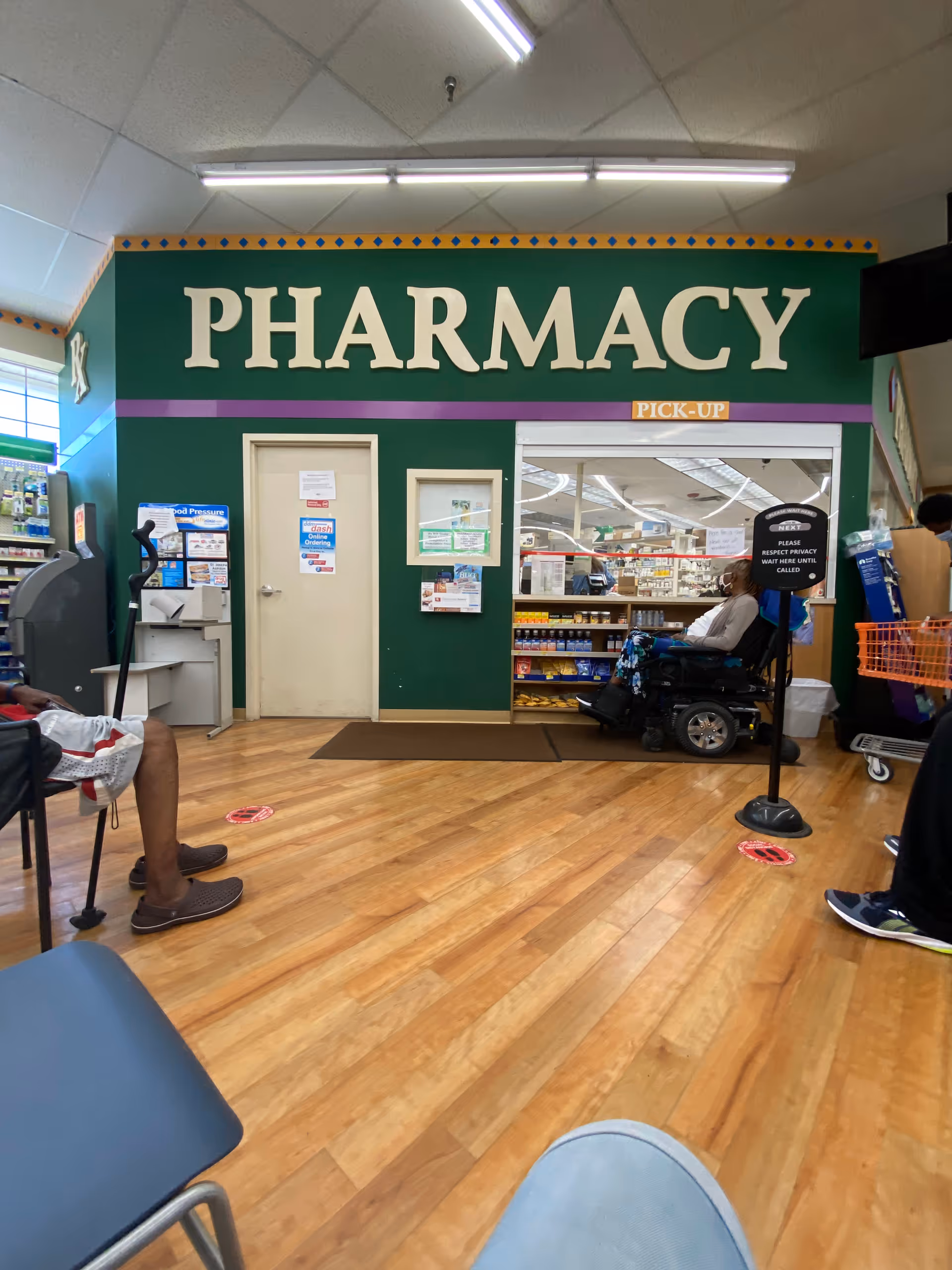 Pharmacy storefront inside a facility with a wheelchair user and seated customers.