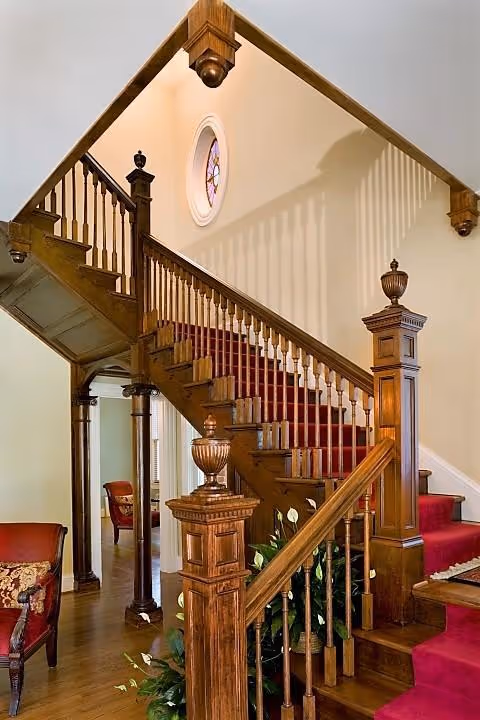 Elegant carved wooden staircase with red carpet in a hospice building foyer.