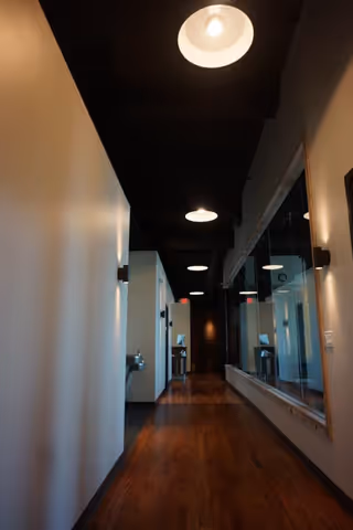 Long hallway with wood floor, white walls, ceiling lights, and glass doors.