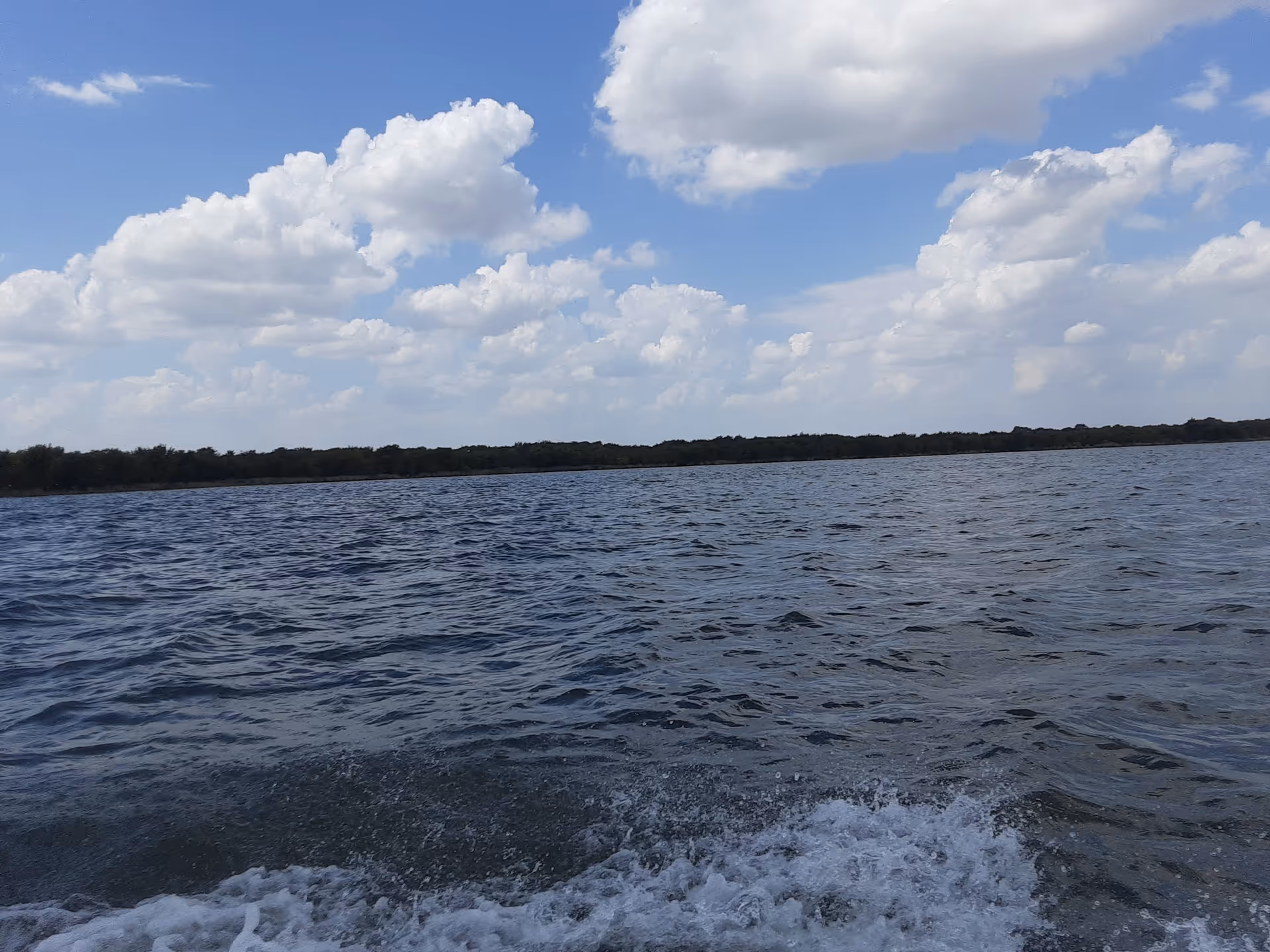 Blue lake with distant shoreline and a partly cloudy sky.
