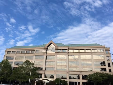 Exterior of a modern multi-story building with large glass windows under a blue sky.