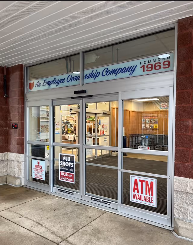 Glass storefront entrance of a drugstore with ATM sign and interior visible.