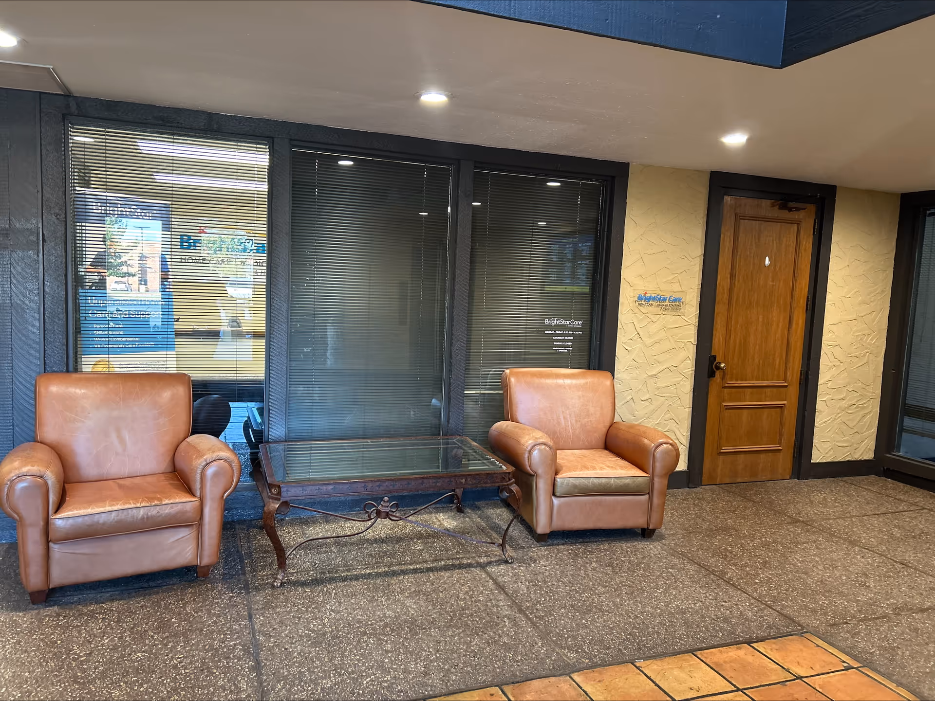 Two brown leather armchairs flank a glass coffee table in a BrightStar Care lobby.