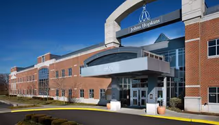 Brick exterior with Johns Hopkins entrance canopy and glass doors under a blue sky.