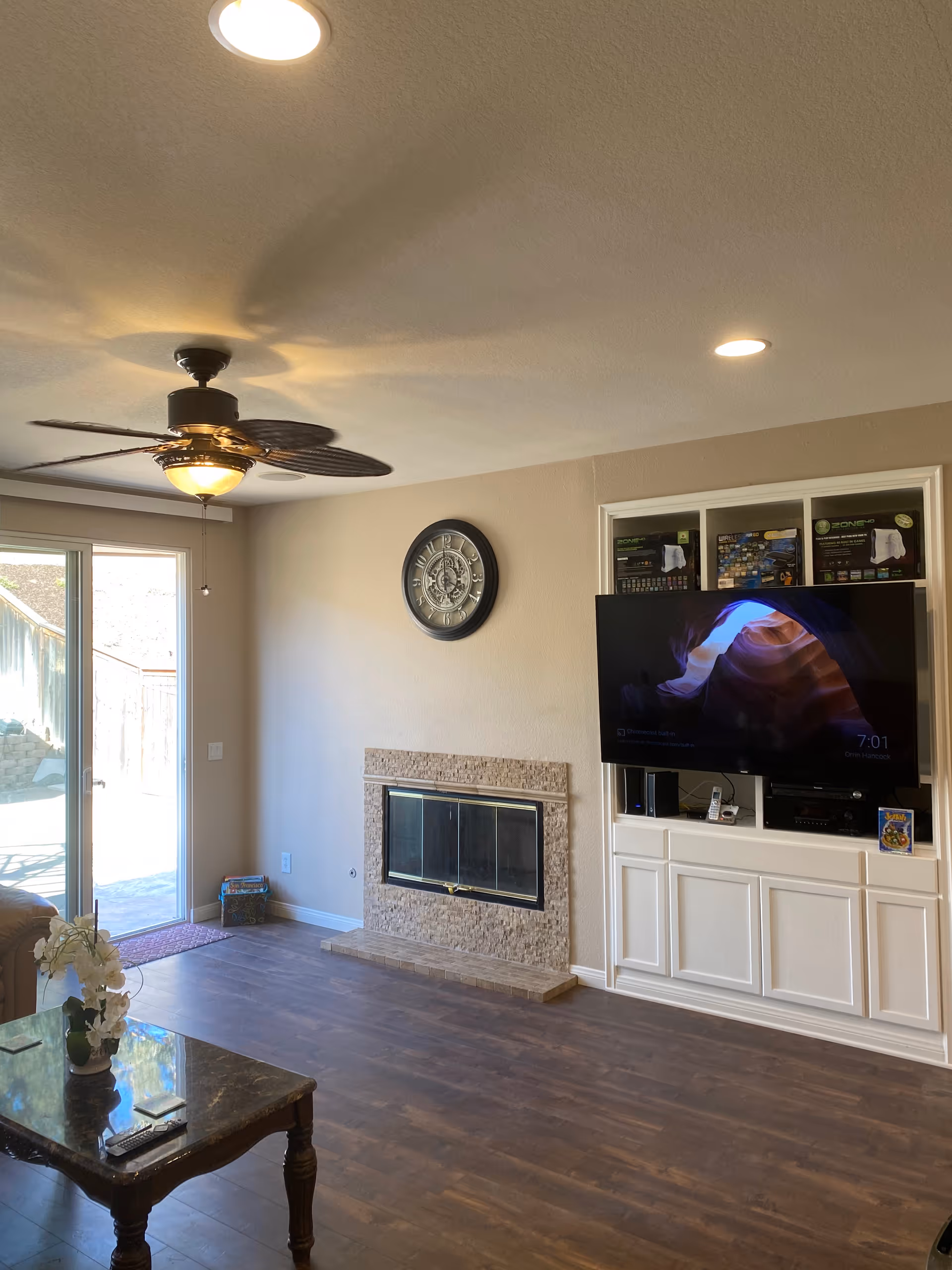 Living room with fireplace, mounted TV, wall clock, ceiling fan, and sliding glass door.
