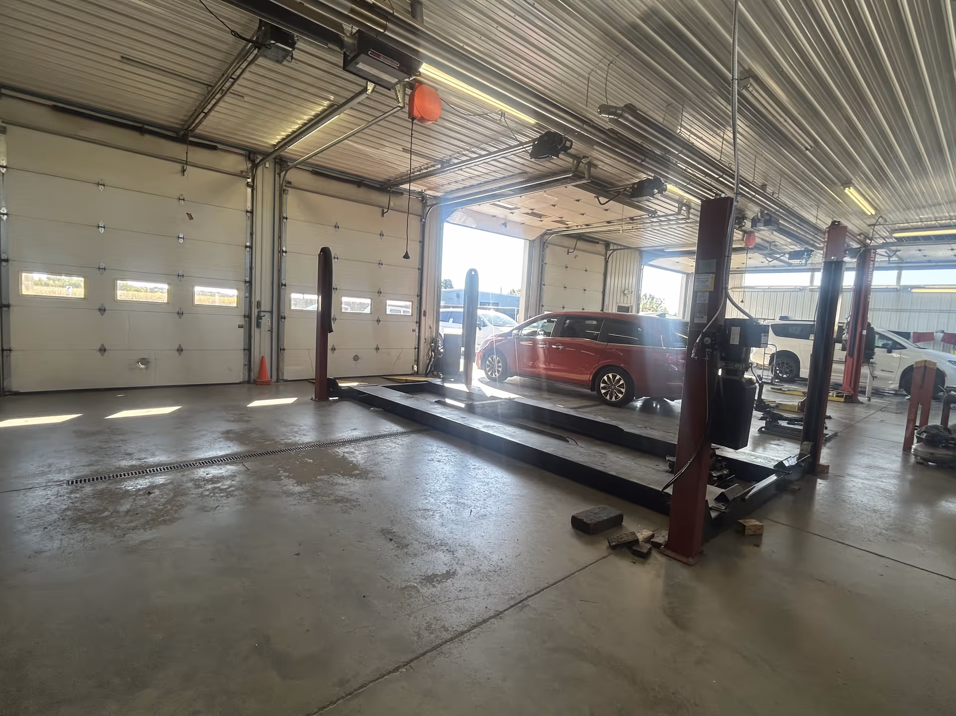 An indoor auto repair shop with a red minivan on a two-post lift.
