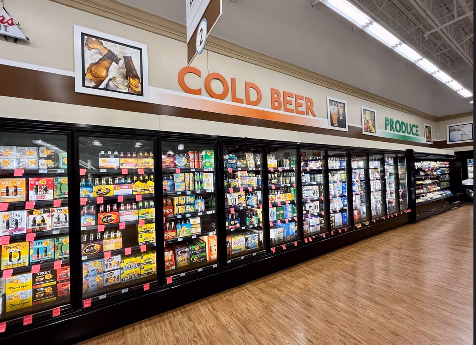 Long row of refrigerated display cases inside a discount drug store with cold beer signage.