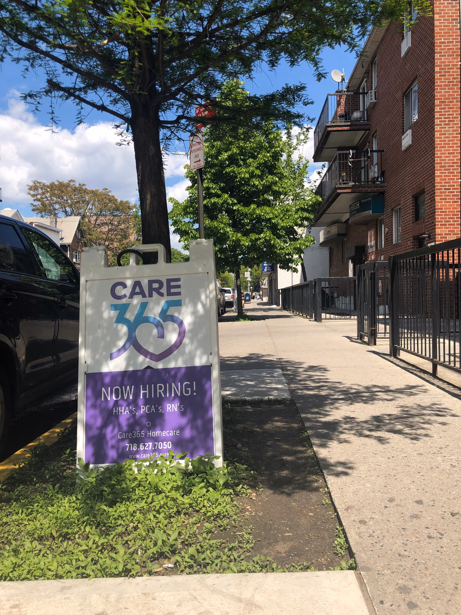 Outdoor sidewalk sign for Care365 Homecare advertising now hiring near a brick building.