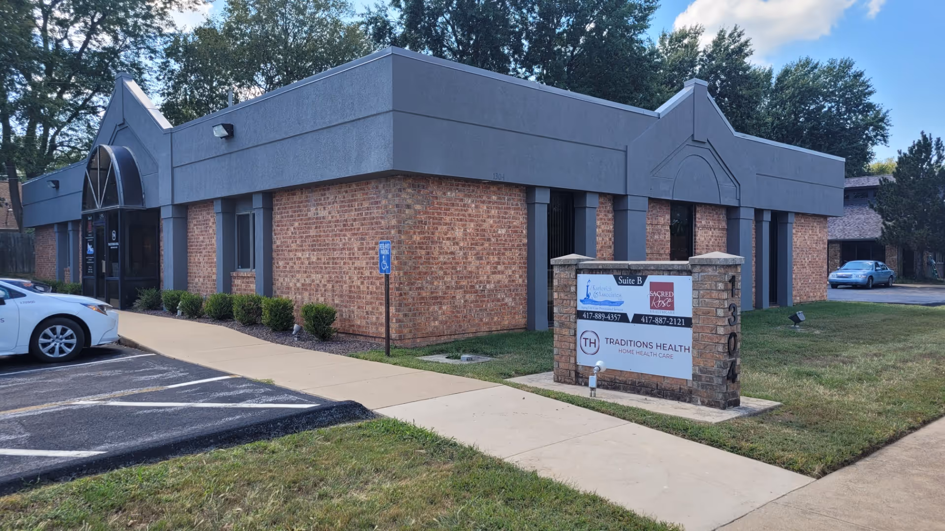 Front exterior of Sacred Rose Healthcare building with brick walls and parking.