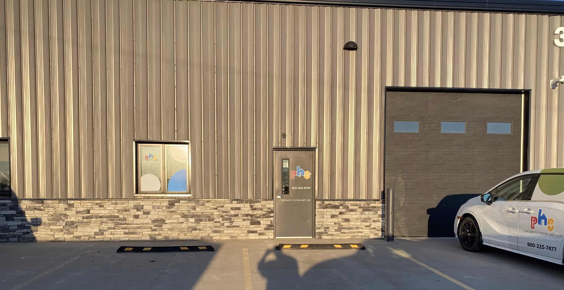 Industrial metal building facade with a small entrance, large garage door, and pediatric home service van.