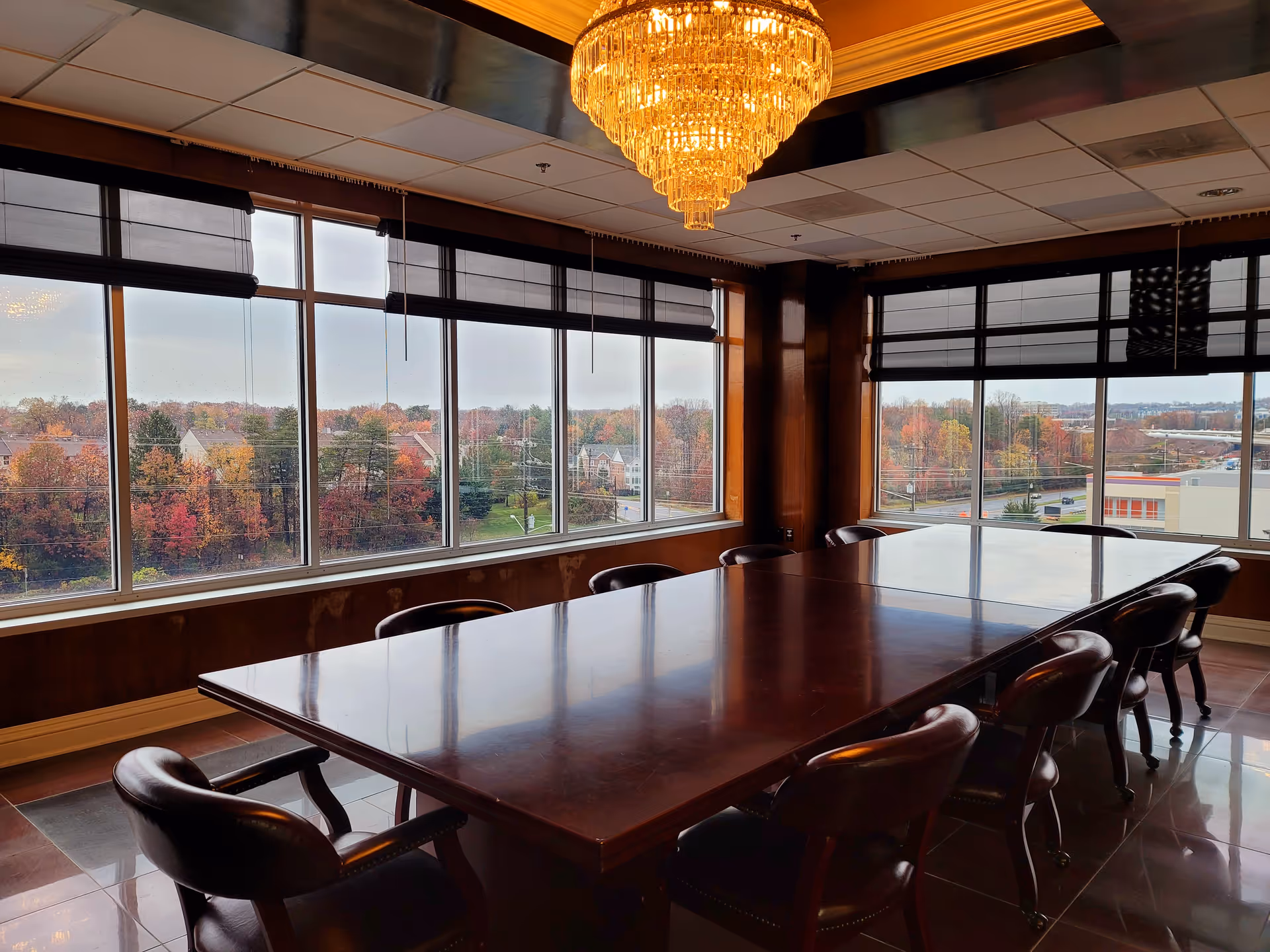 A long polished conference table with chairs in a bright windowed meeting room with a chandelier