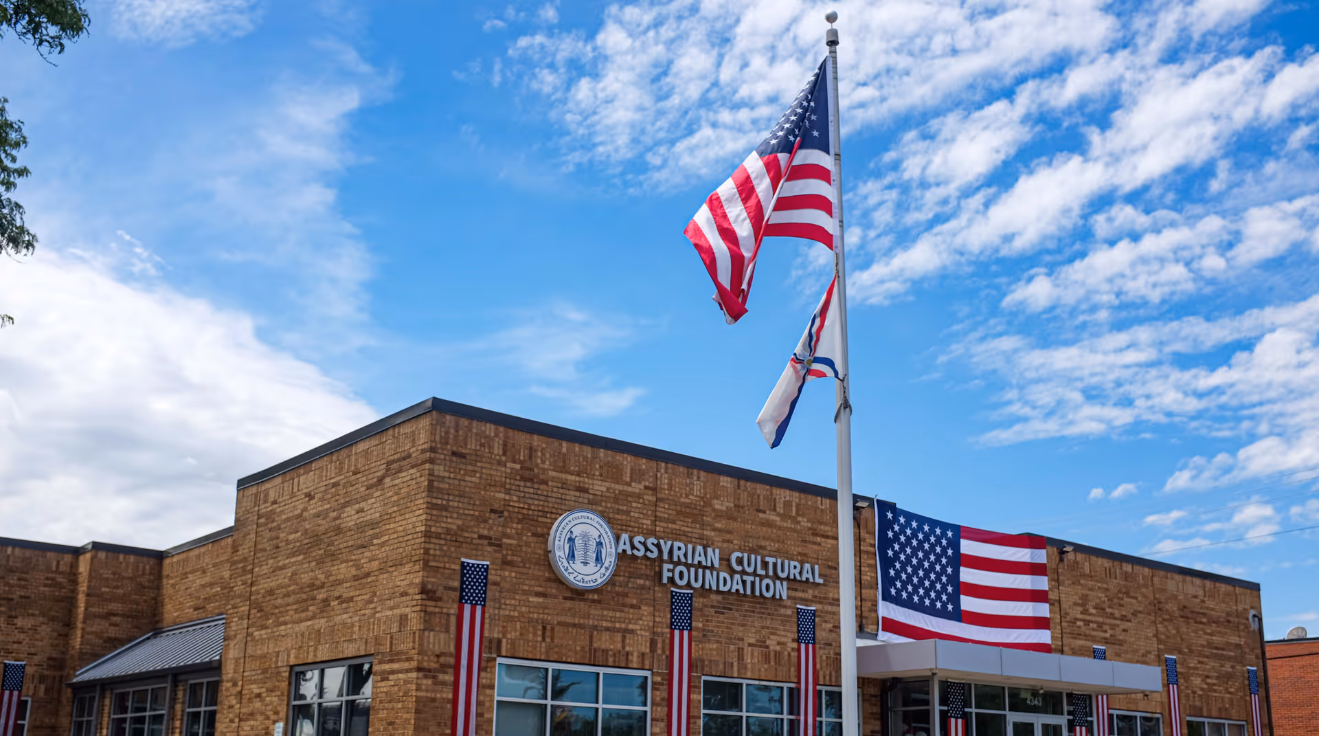 Exterior brick building front with flags and circular emblem under blue sky.